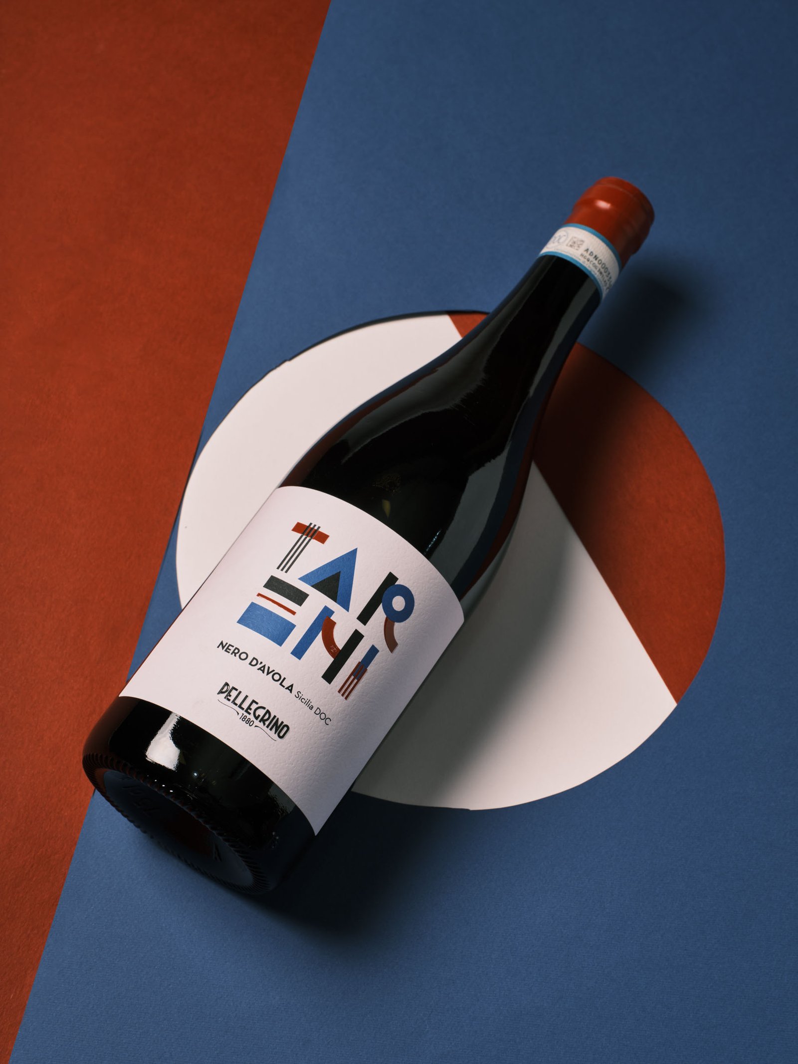 Pellegrino Tarì Nero d'Avola coricata su fondi rosso e blu con un disco bianco