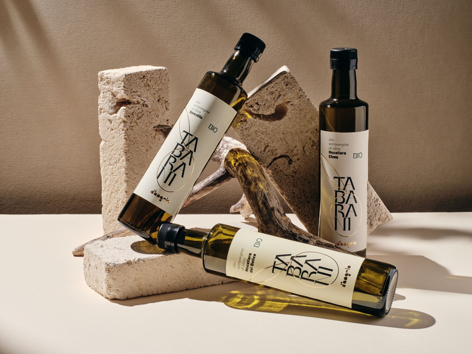 Tre bottiglie di olio Tabarani d'Angelo fra blocchi di pietra e legno di mare