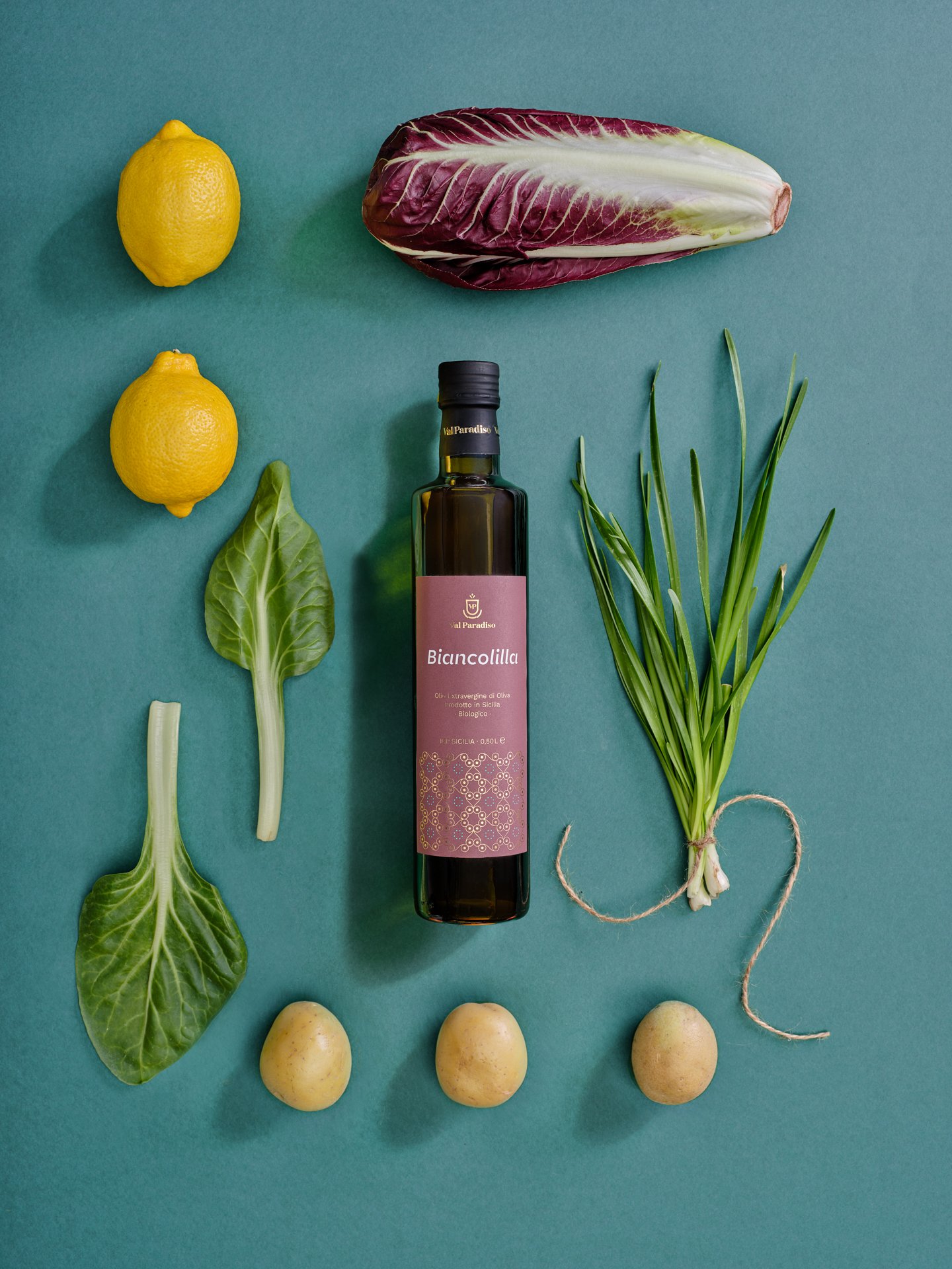 Olio Val Paradiso Biancolilla al centro di verdure e limoni disposti su fondo verde
