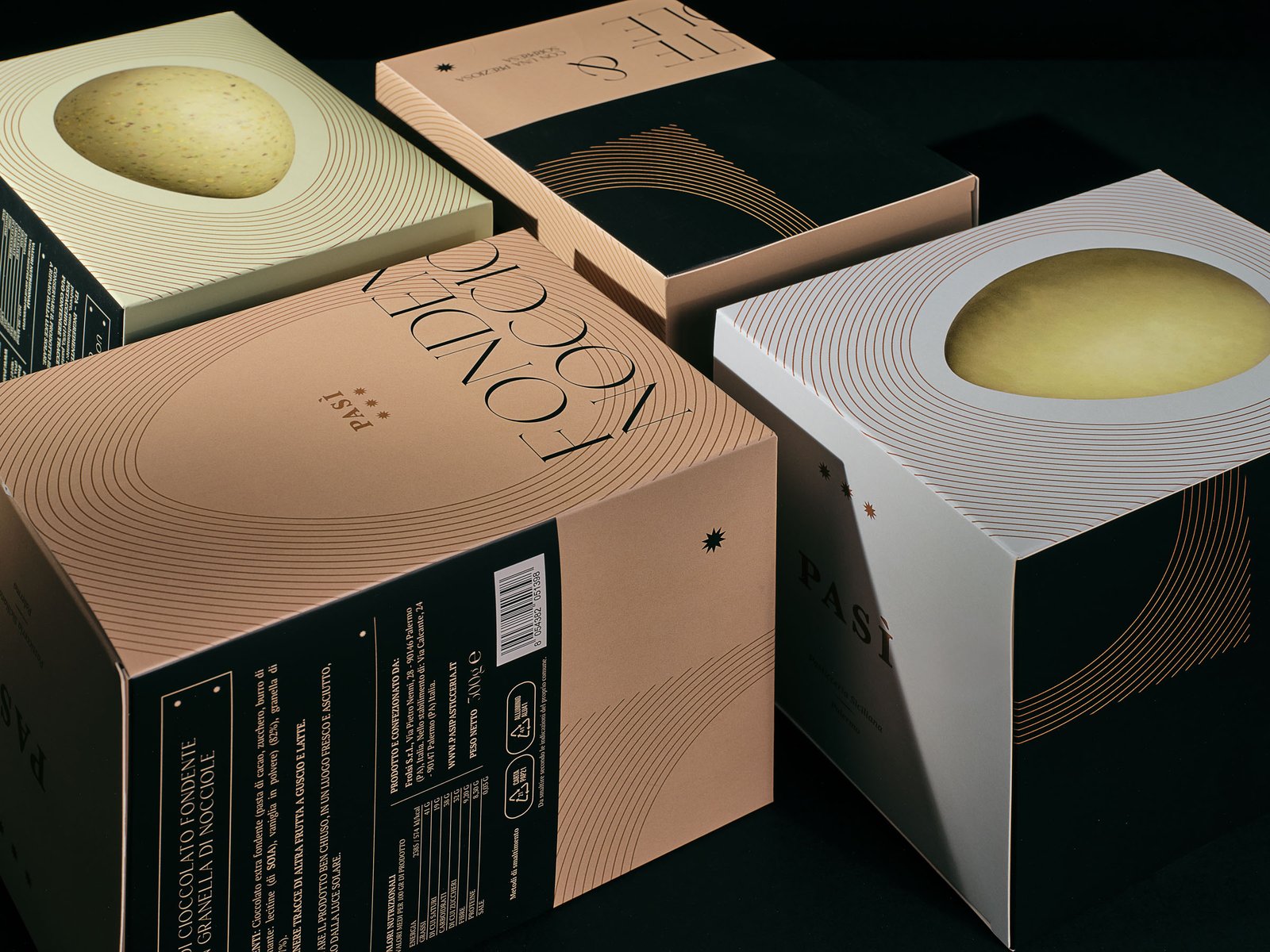 Pasì Easter egg boxes on a black set: Fondente & Nocciole in powder pink, Pistacchio & Granella in pale green and Cioccolato al pistacchio in white, with the egg on the lid and fine copper lines