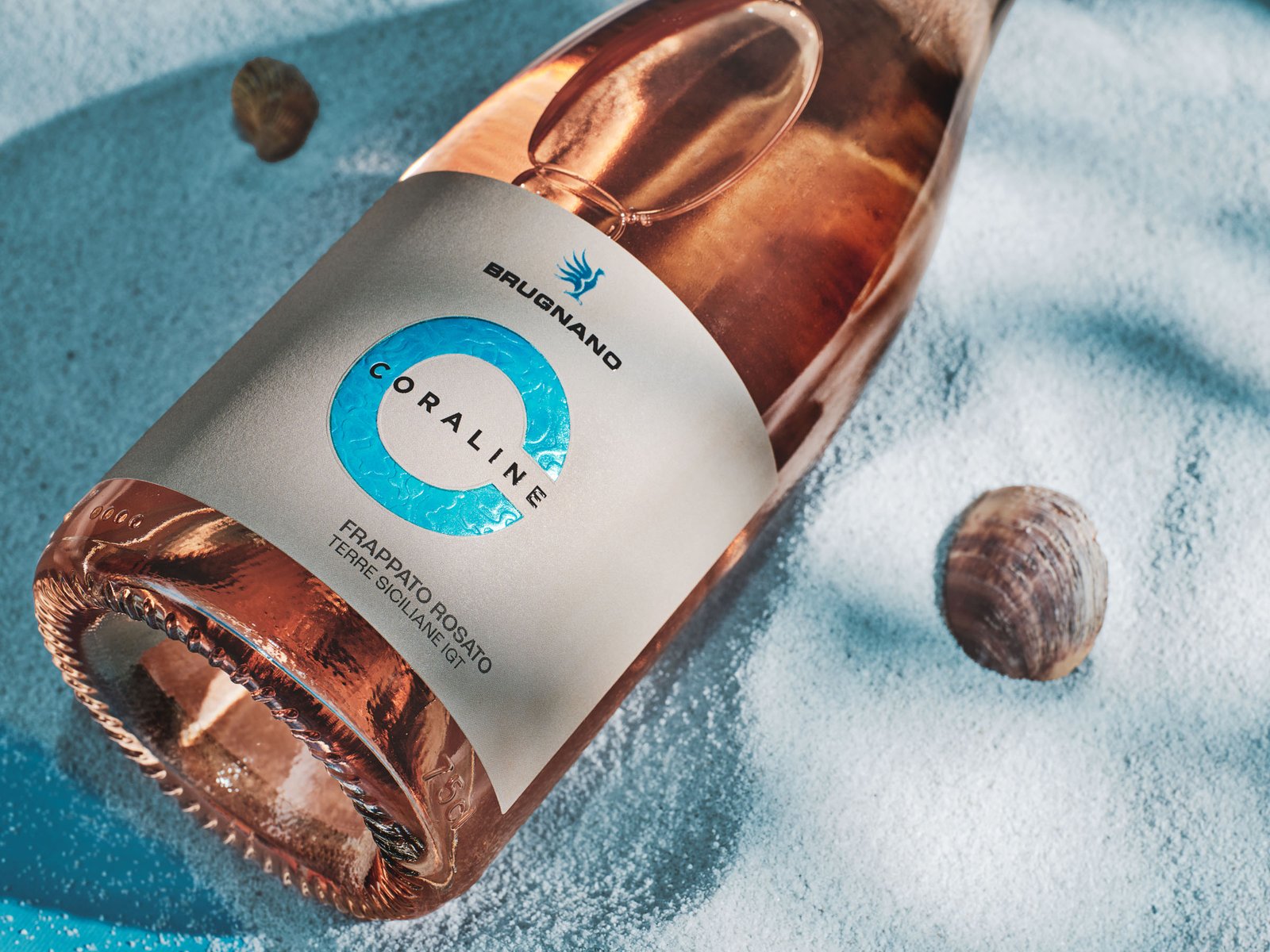 Coraline Frappato rosé lying on blue sand with two shells