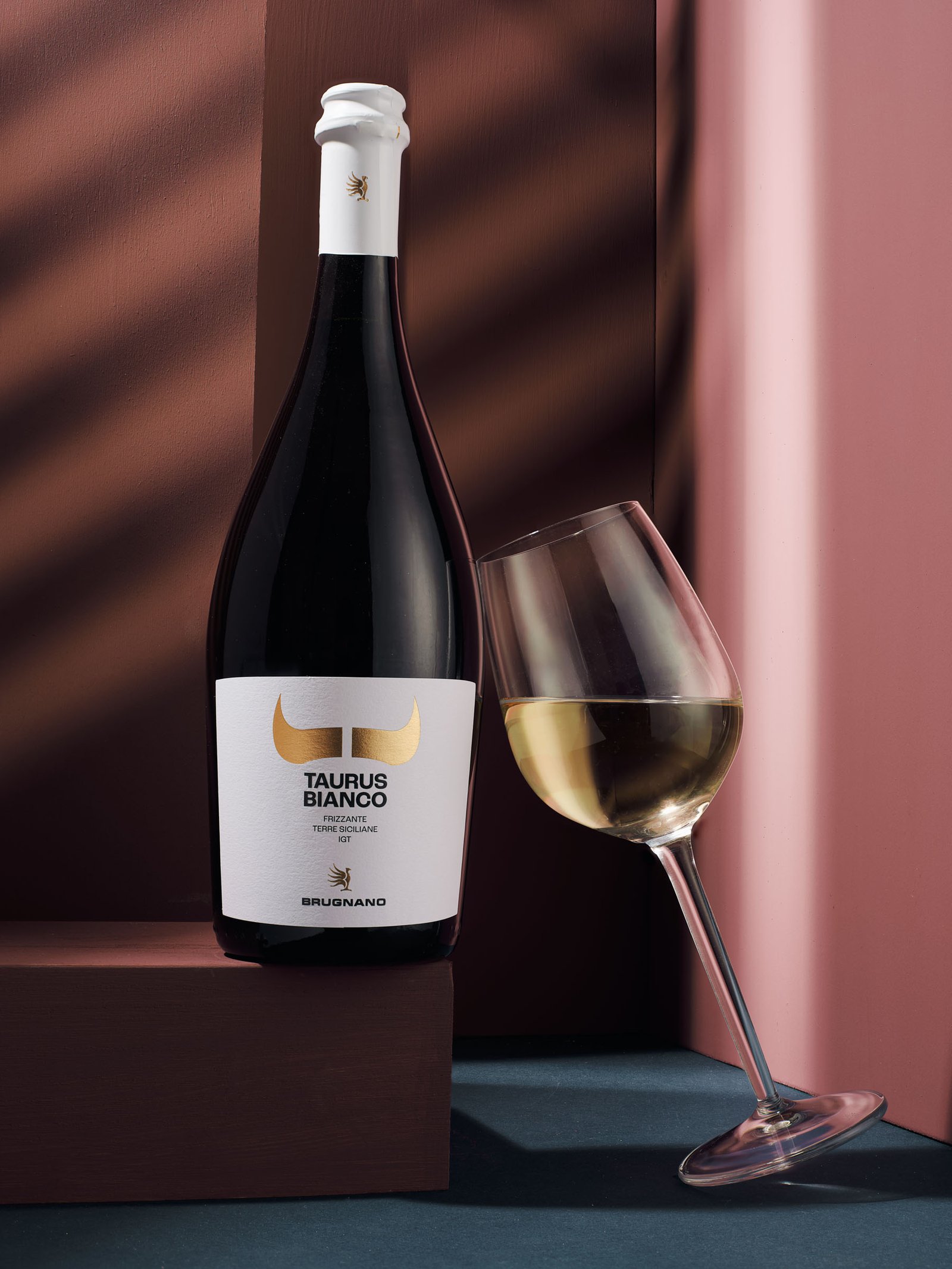 Taurus Bianco frizzante and a glass on a terracotta and dusty pink ground