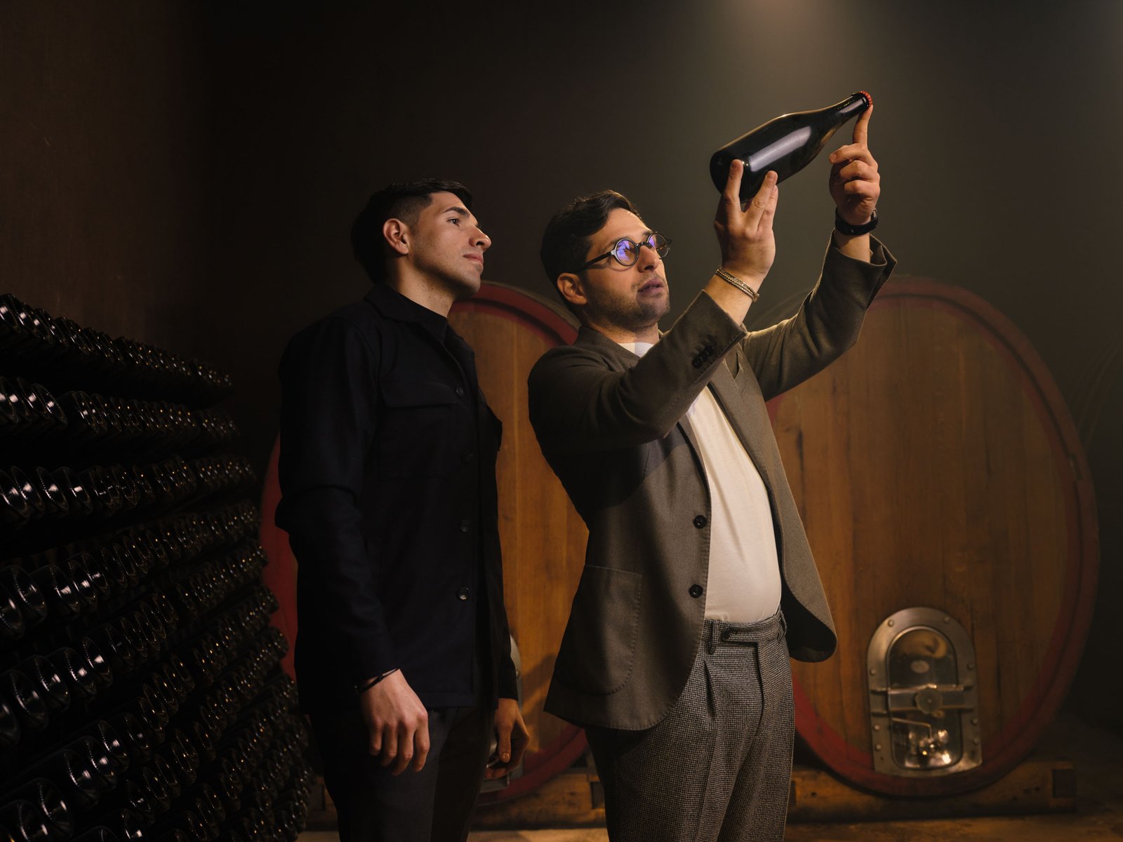 One owner lifts the bottle towards the light, the other watches