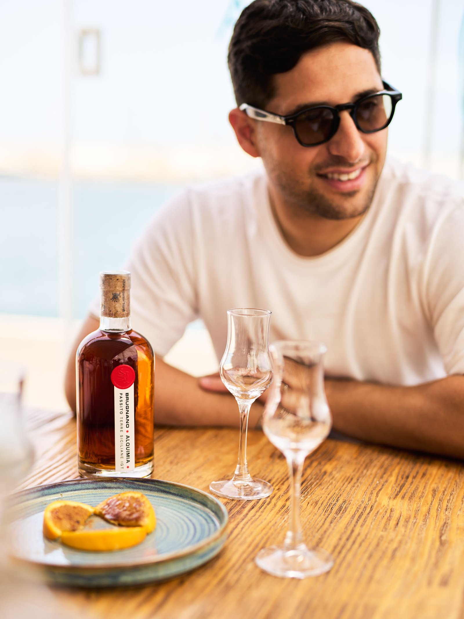 At the table with the Alquimia and the small glasses, the sea behind
