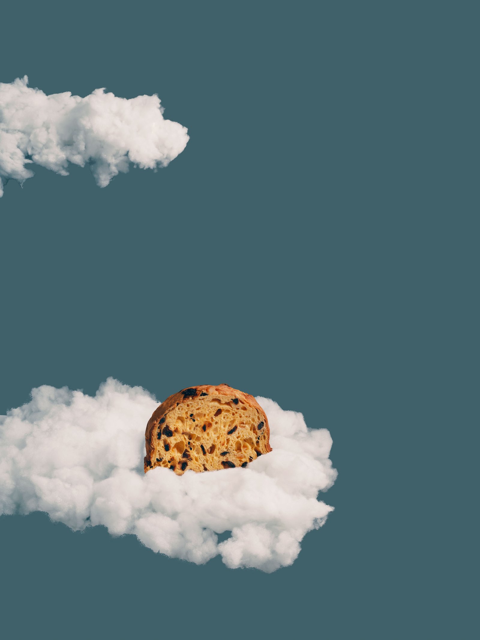 Fetta di panettone posata su una nuvola, cielo grigio-azzurro: immagine di campagna
