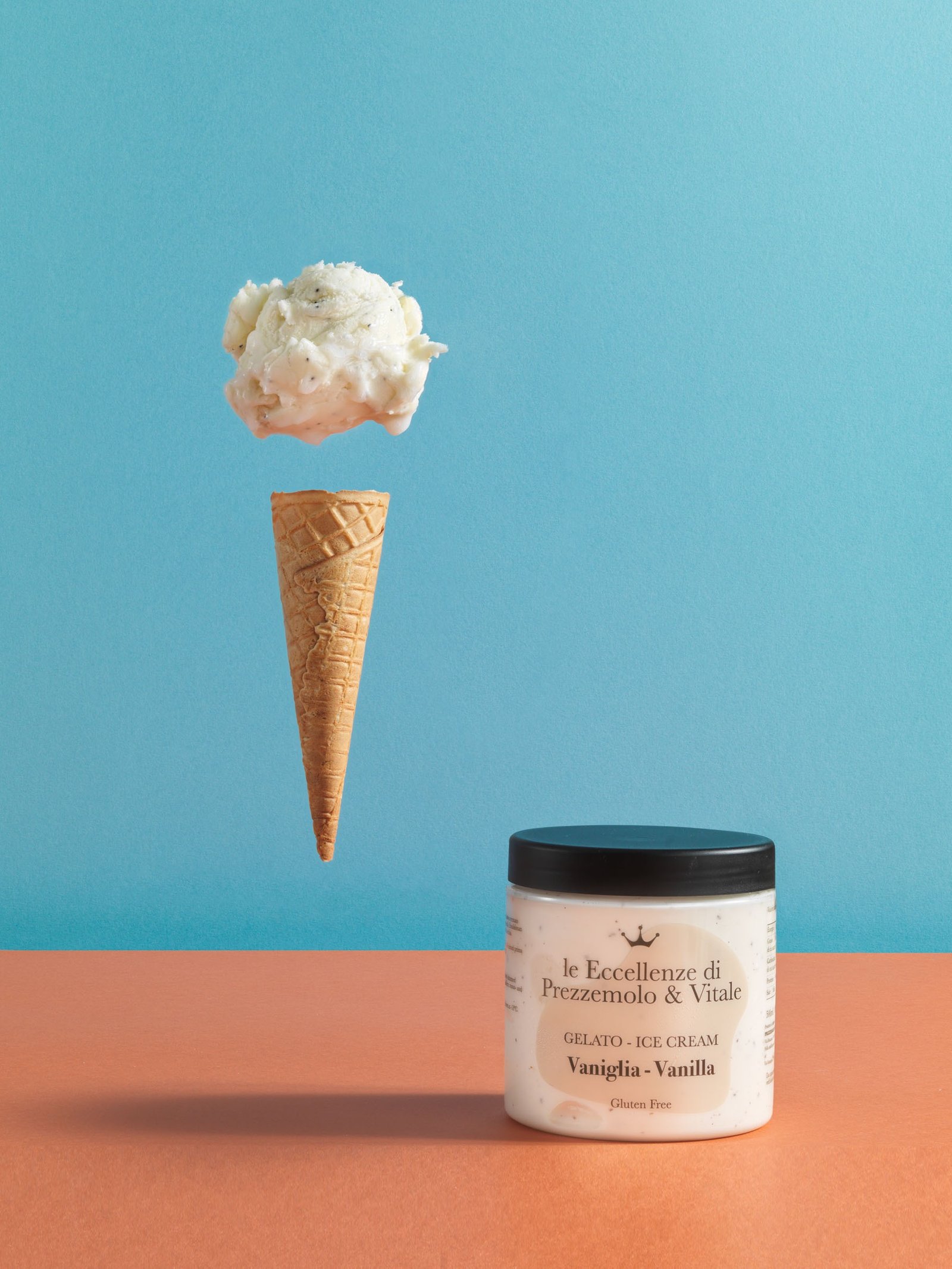 Barattolo di gelato alla vaniglia «le Eccellenze di Prezzemolo & Vitale» su un piano arancio, con una pallina e un cono sospesi sopra, su fondo azzurro