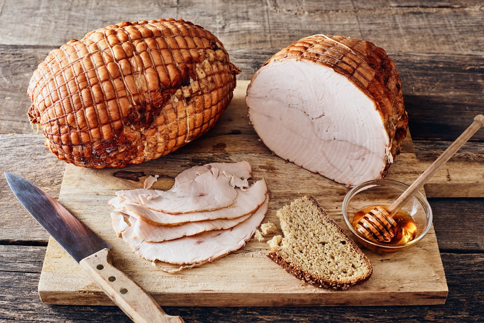 Un pezzo intero con i segni della rete e la sua metà aperta, le fette sottili sul tagliere, il pane e una ciotola di miele