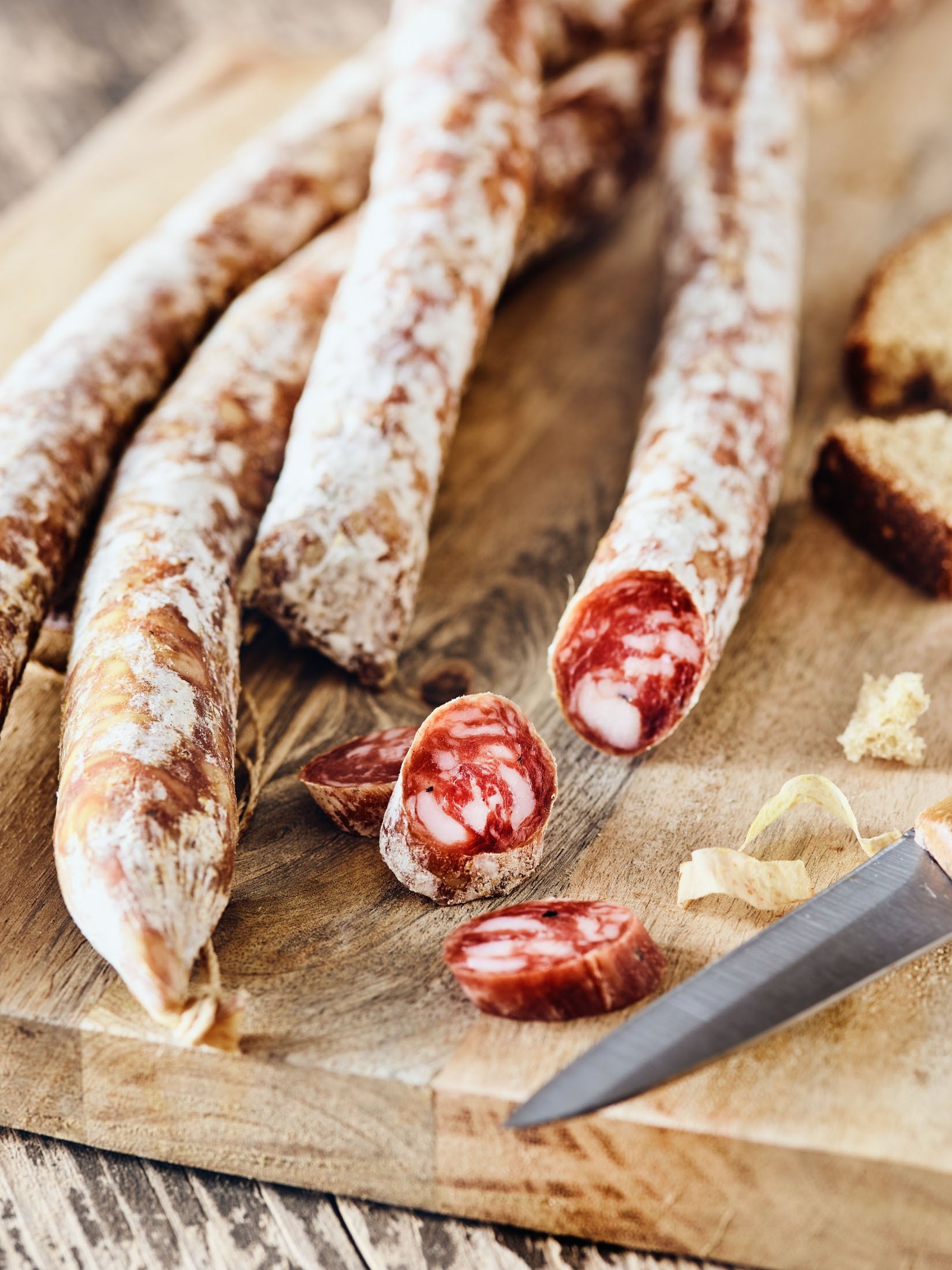 Salumi lunghi e sottili sul tagliere, uno tagliato a rondelle, con il pane e il coltello