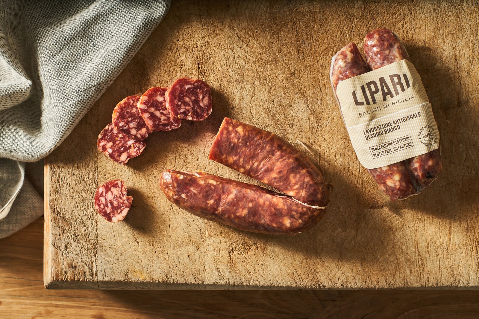 Salame intero nella fascetta di carta Lipari, mezzo salame e fette su un tagliere di legno