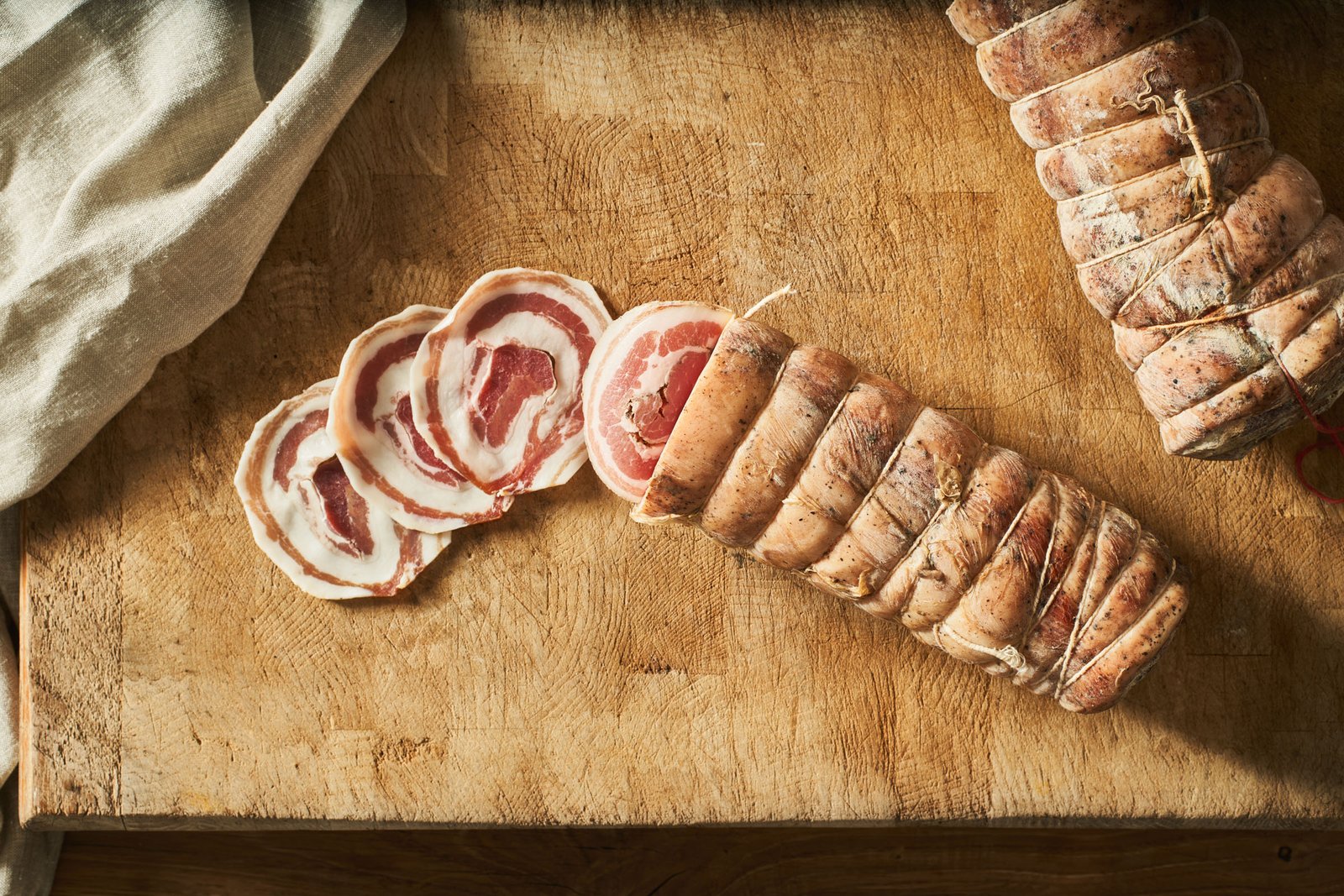 Fette di pancetta coppata arrotolate a spirale accanto ai pezzi interi legati con lo spago