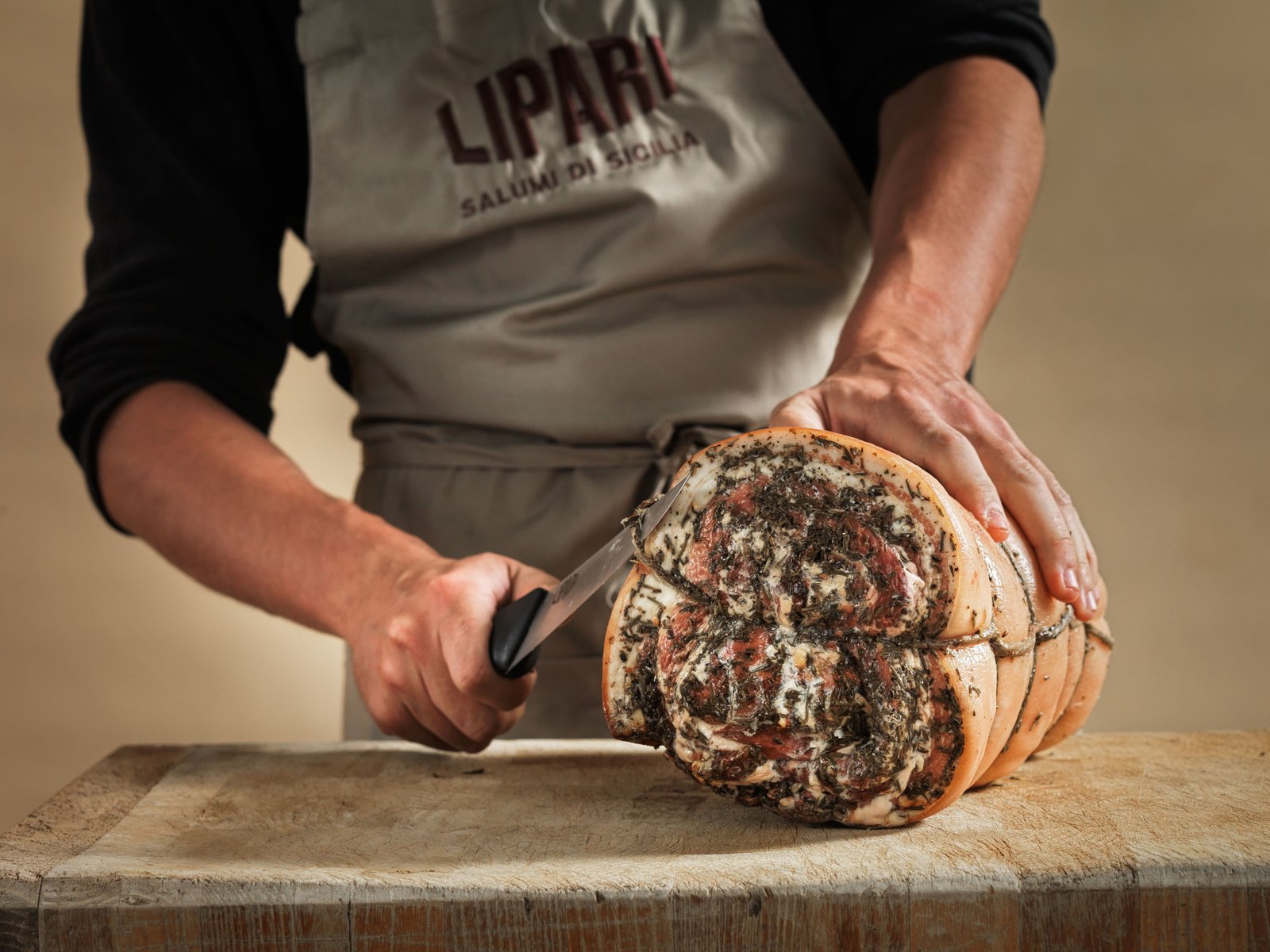 Un grembiule Lipari e le mani che affettano una porchetta arrotolata alle erbe