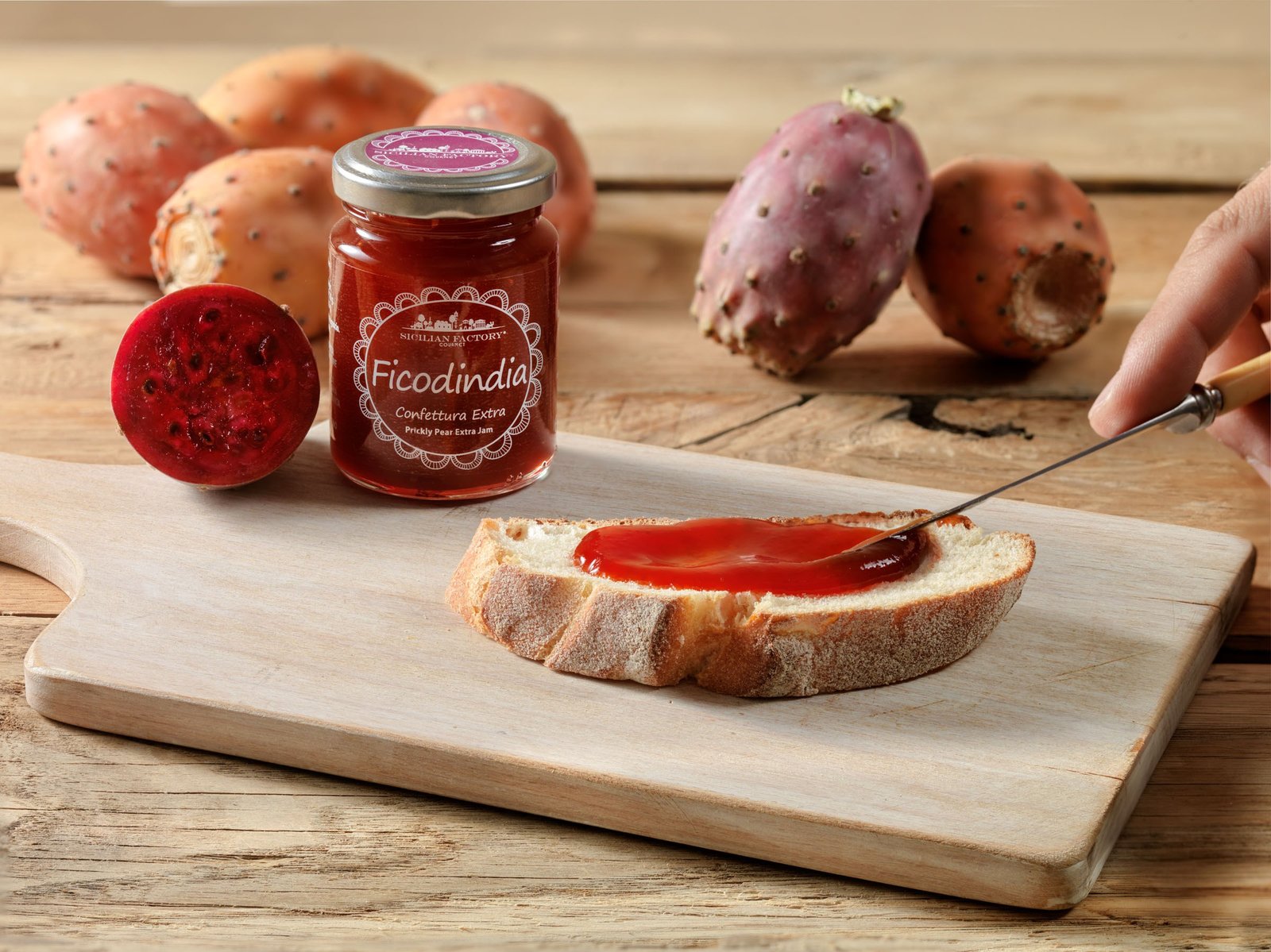 Prickly pear extra jam on a board: a hand spreads it on a slice of bread, with whole prickly pears around and one cut in half