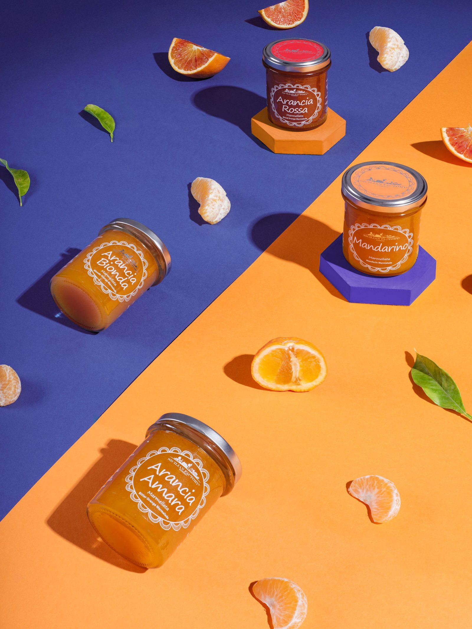 Blood orange, mandarin, blonde orange and bitter orange marmalades on a background split between blue and orange, with citrus segments and leaves