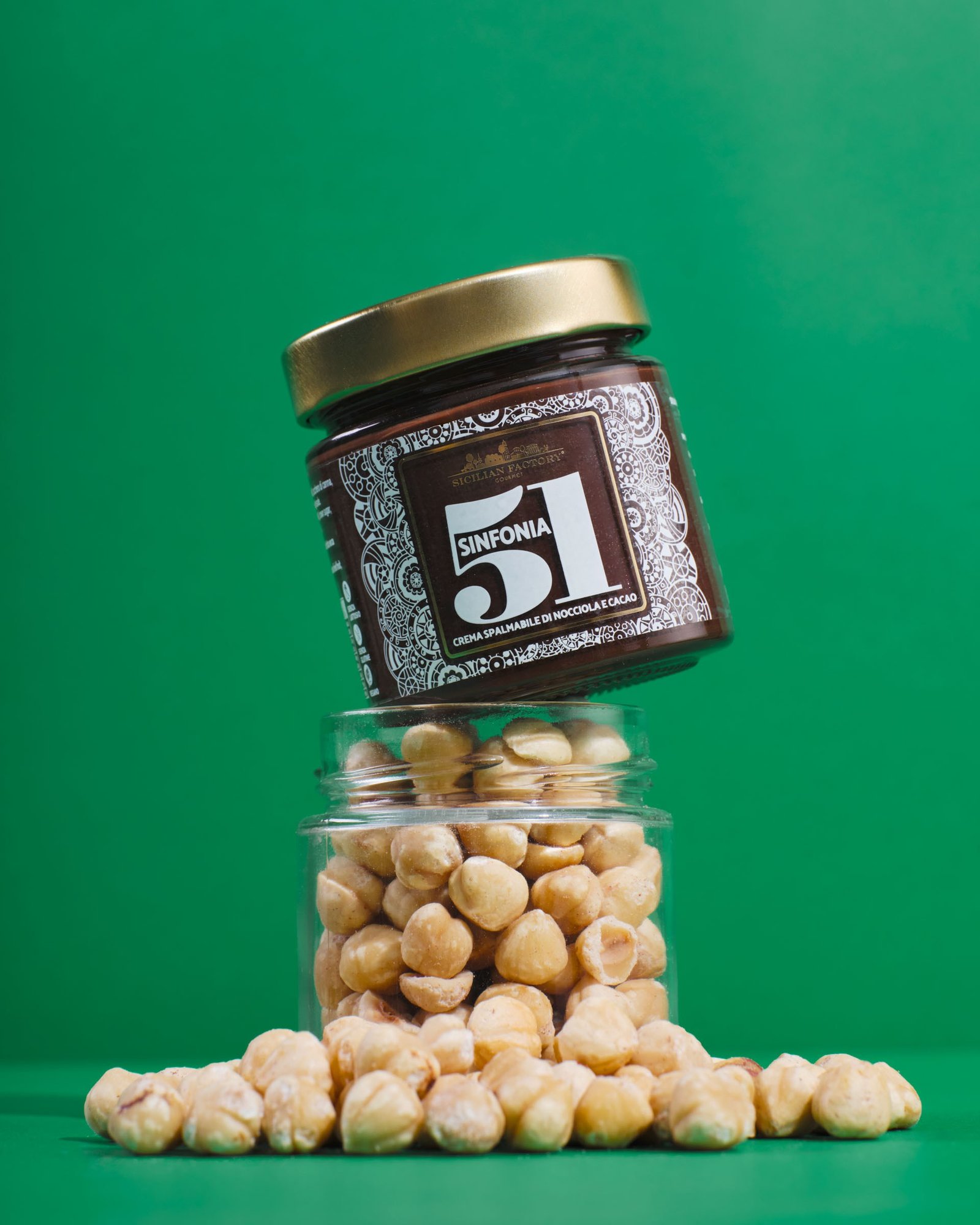 Sinfonia 51 hazelnut and cocoa spread balanced on a glass jar full of hazelnuts, on a green background