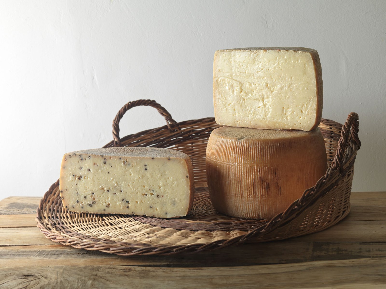 Pecorino stagionato intero con uno spicchio appoggiato sopra, e mezza forma di pecorino pepato, in un vassoio di vimini