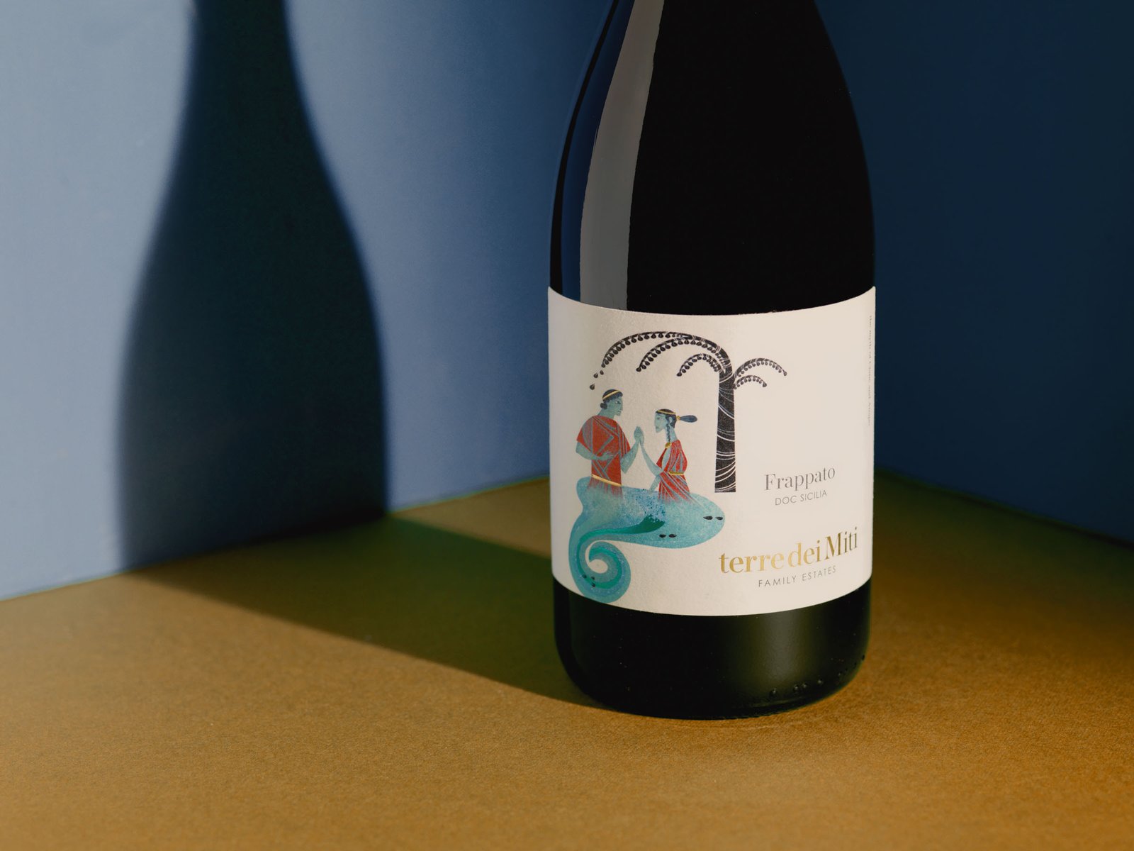 Terre dei Miti Frappato on an ochre surface between blue walls, in hard light that throws the bottle's shadow onto the wall