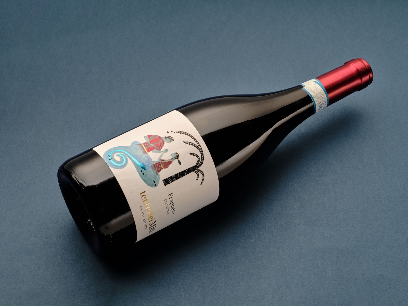 Terre dei Miti Frappato lying on blue paper, with its red capsule and the Ciane and Anapo label